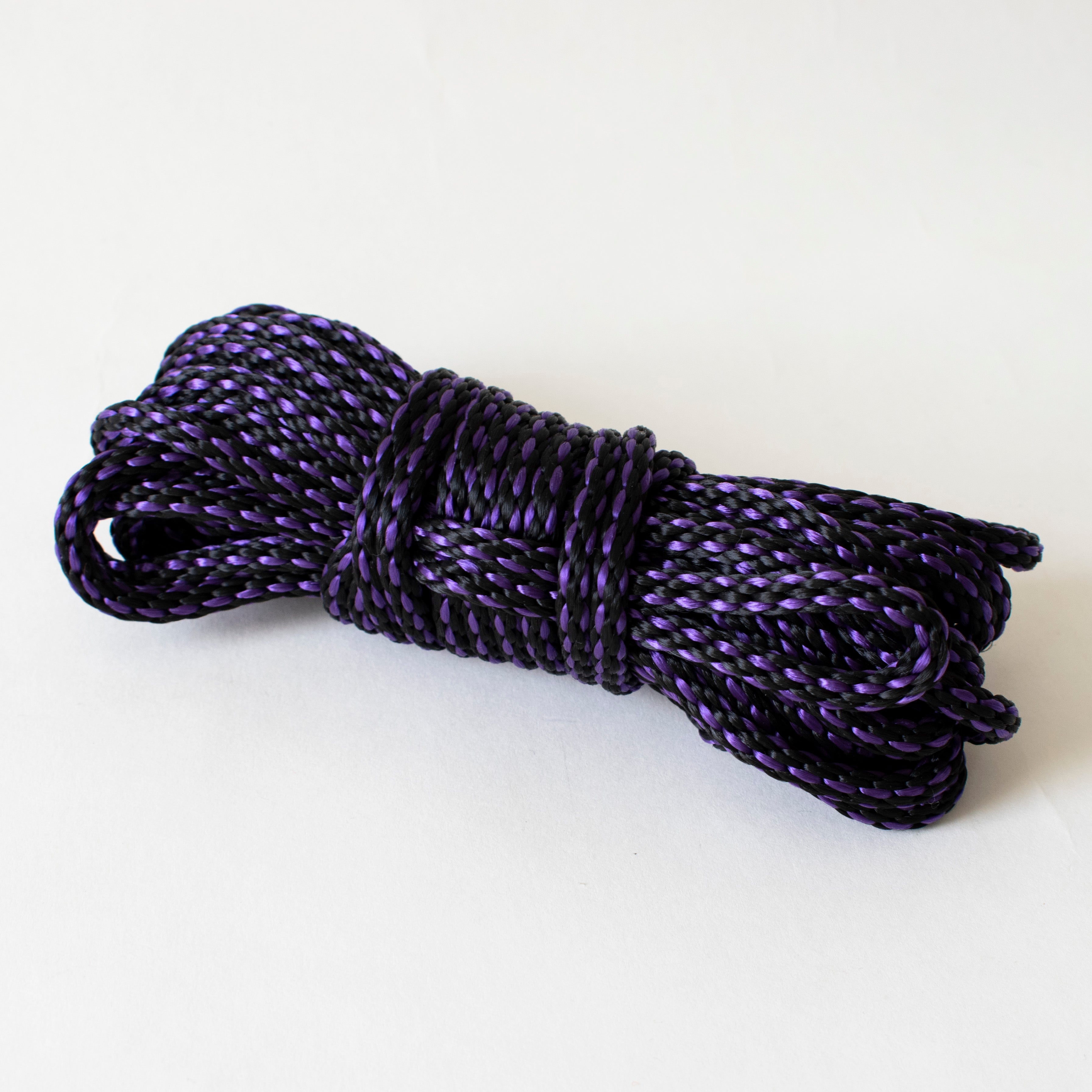 Purple and black 1/4-inch (6mm) solid braid MFP rope from Agreeable Agony bondage rope kit, shown in a coiled bundle.